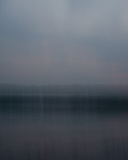 a grey, intentionally blurred view of a lake in the evening
